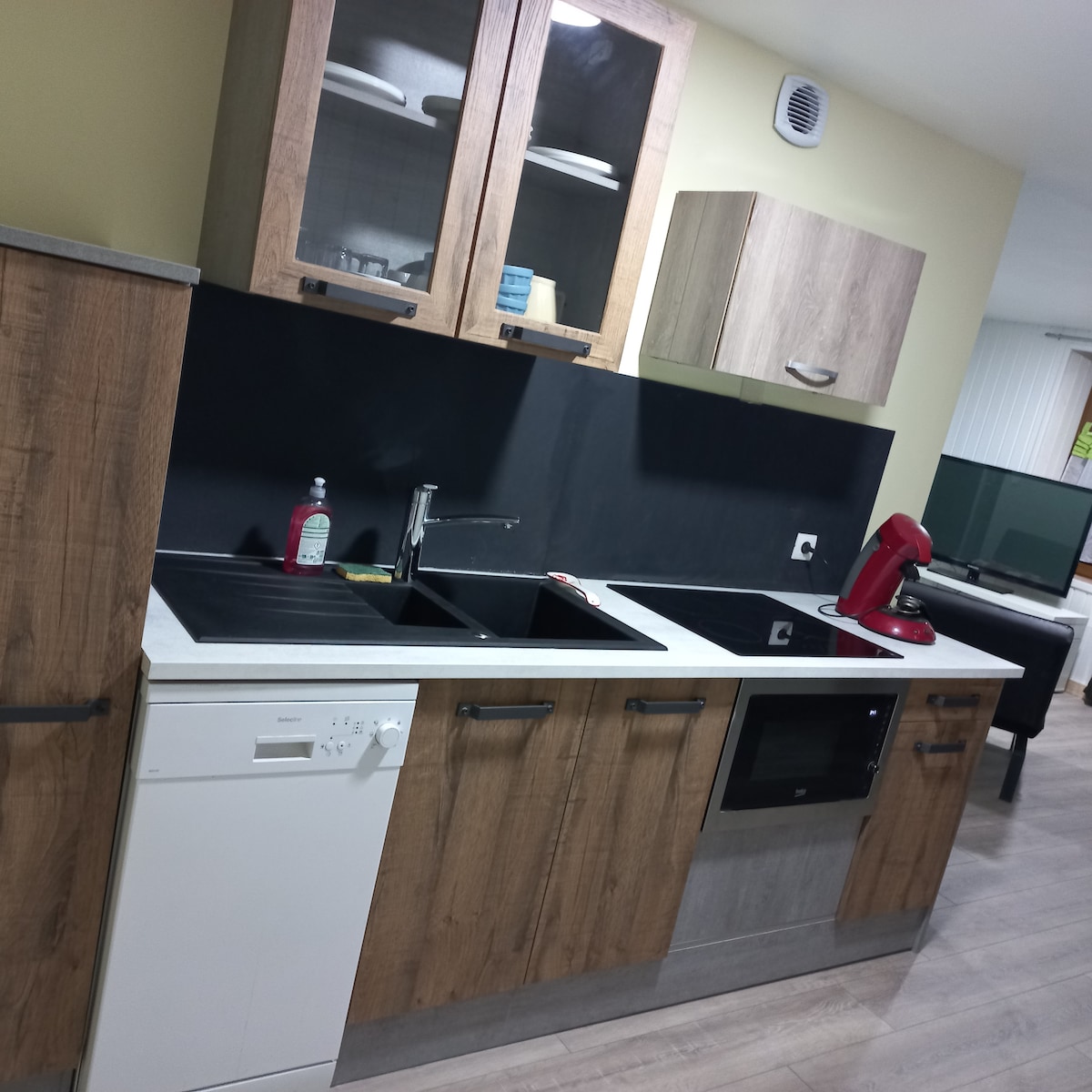 The kitchen area features a modern layout with wood cabinetry and sleek countertops. A dishwasher and built-in oven are included, along with a double sink. Open shelving holds dishware, while an appliance stand hosts a stand mixer, providing convenience for cooking and meal prep.