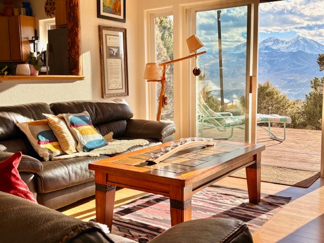 A bright living area is showcased with comfortable leather sofas, accented by colorful throw pillows. A wooden coffee table is positioned in front, while large glass doors reveal expansive mountain views and access to the outdoor deck.