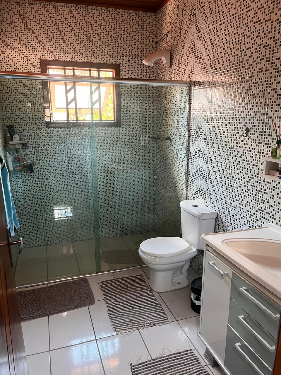 The bathroom features a glass shower enclosure and modern fixtures, including a toilet and a sleek sink with storage. White tiles and patterned walls create a clean aesthetic. Natural light enters through a window, enhancing the overall brightness of the space.