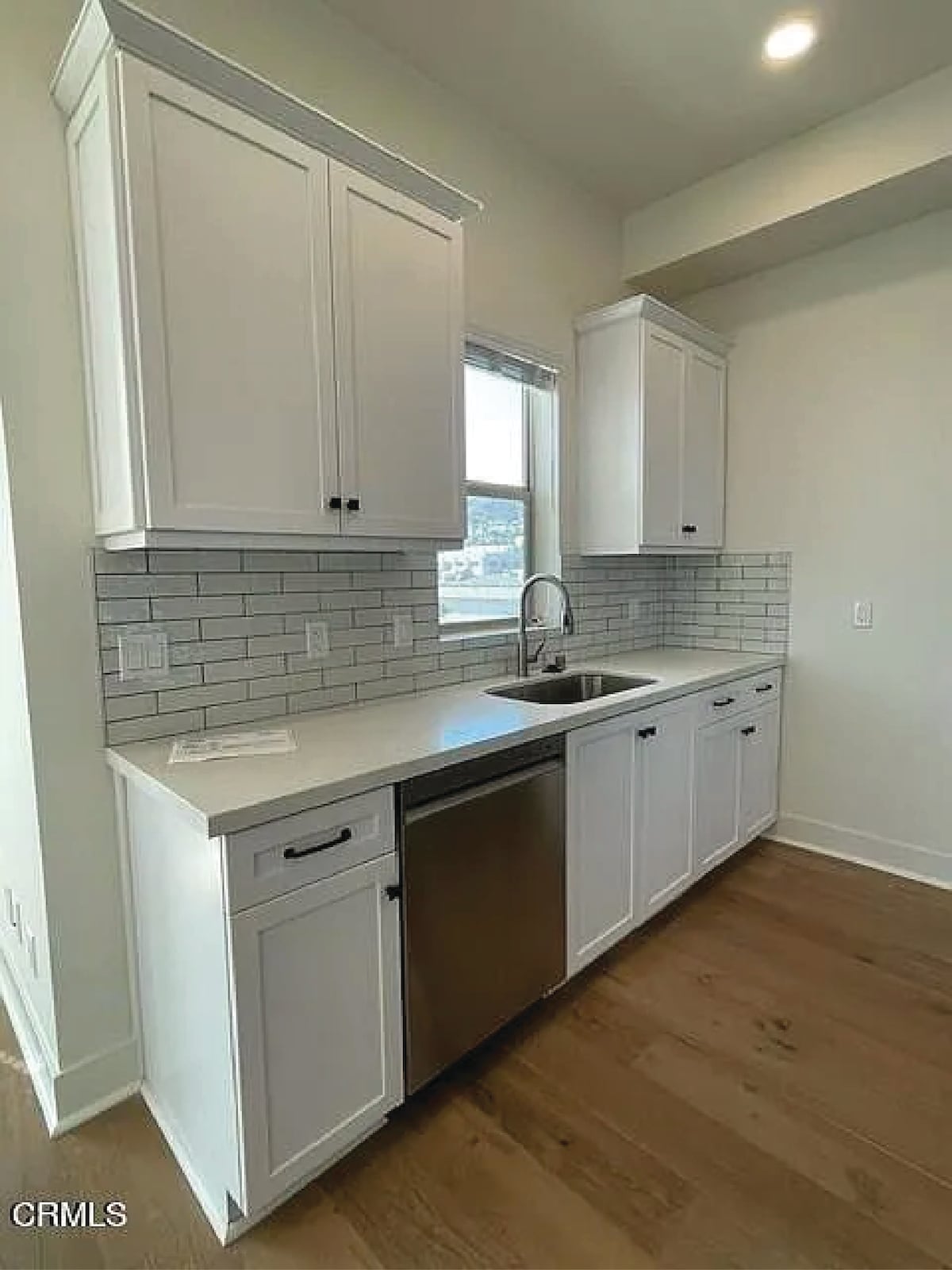 A modern kitchen area is featured, showcasing sleek white cabinetry and a stainless steel sink. A window allows natural light to illuminate the space, which is accented by a tiled backsplash. The countertops are smooth and minimalistic, enhancing the kitchen's functional design.