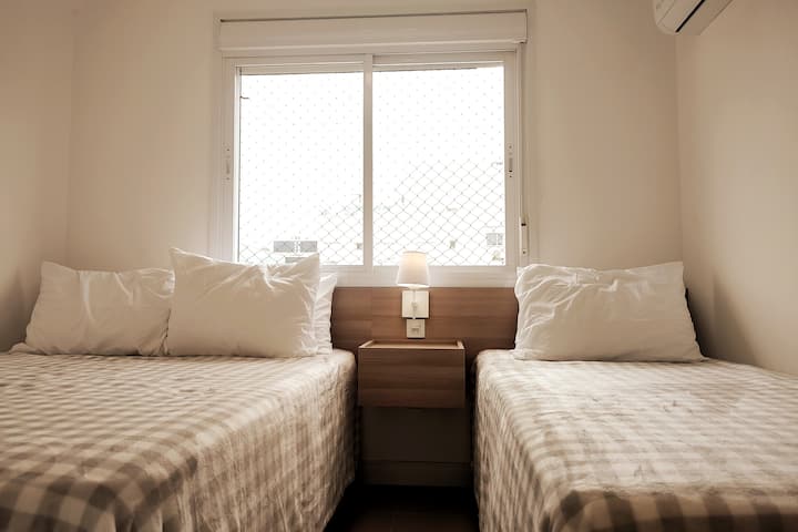 Habitación social con una cama doble y una cama individual, aire acondicionado, una ventana con una pantalla protectora y un gran armario para el almacenamiento. Sábanas, mantas y almohadas disponibles para usar durante tu estadía.