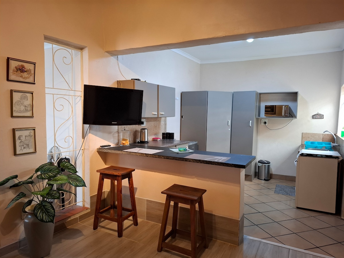 A modern kitchen area is presented, featuring stainless steel appliances, including two large refrigerators. A countertop with bar stools provides a casual dining space. A large window allows natural light to brighten the room, complemented by decorative art on the wall.