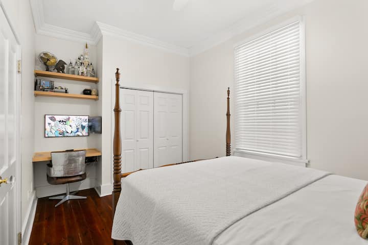 Helles Gästezimmer mit einem gemütlichen Himmelbett und einem eigenen Arbeitsbereich. Perfekt für Remote-Arbeit, mit einem Monitor und einem Schreibtisch, der in ein eingebautes Regal gesteckt ist. Einfach, ruhig und komfortabel.