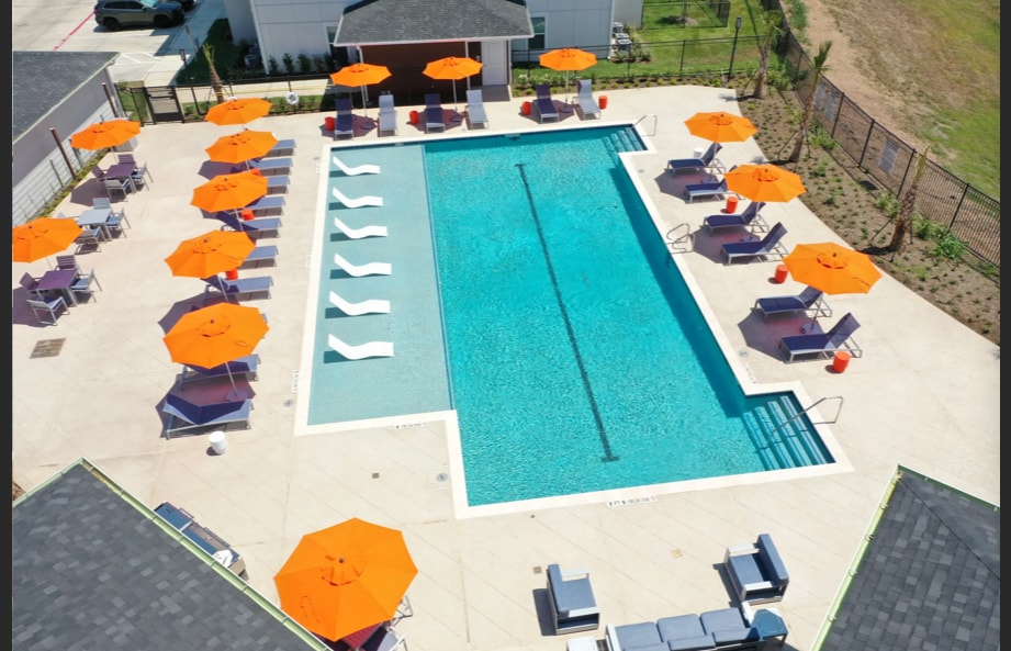 A spacious outdoor swimming pool is surrounded by lounge chairs and bright orange umbrellas. The pool features clear, inviting water, with a lane marked for swimming. A well-maintained deck area complements the scene, enhancing the relaxation space.