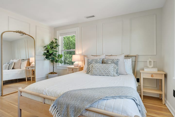 Táto spálňa je pokojná a slnečná a má manželskú posteľ s vrstvenými vankúšmi, mäkkou posteľnou bielizňou a útulným hodom. Užite si elegantné stenové lišty, teplé drevené tóny a veľké zrkadlo ideálne na prípravu.