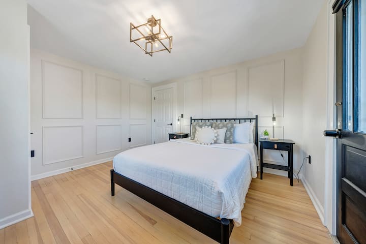 Spálňa s manželskou posteľou s čistými líniami, teplými drevenými podlahami a modernými detailmi stien. Tichý, pohodlný priestor na oddych - či už ste vonku a objavujete alebo sa v ňom ubytujete.