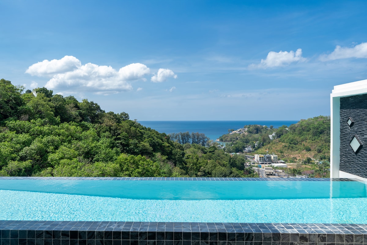 A serene infinity pool stretches gracefully toward the horizon, offering unobstructed views of lush greenery and the sparkling sea. Soft blue waters blend seamlessly with the sky, creating a tranquil space for relaxation and enjoyment of the natural surroundings.