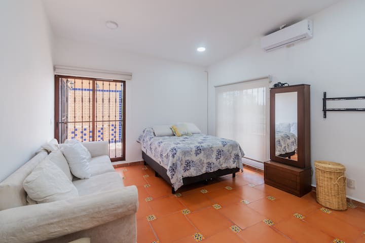 Chambre lumineuse avec climatisation, salon privé et plancher en terre battue.