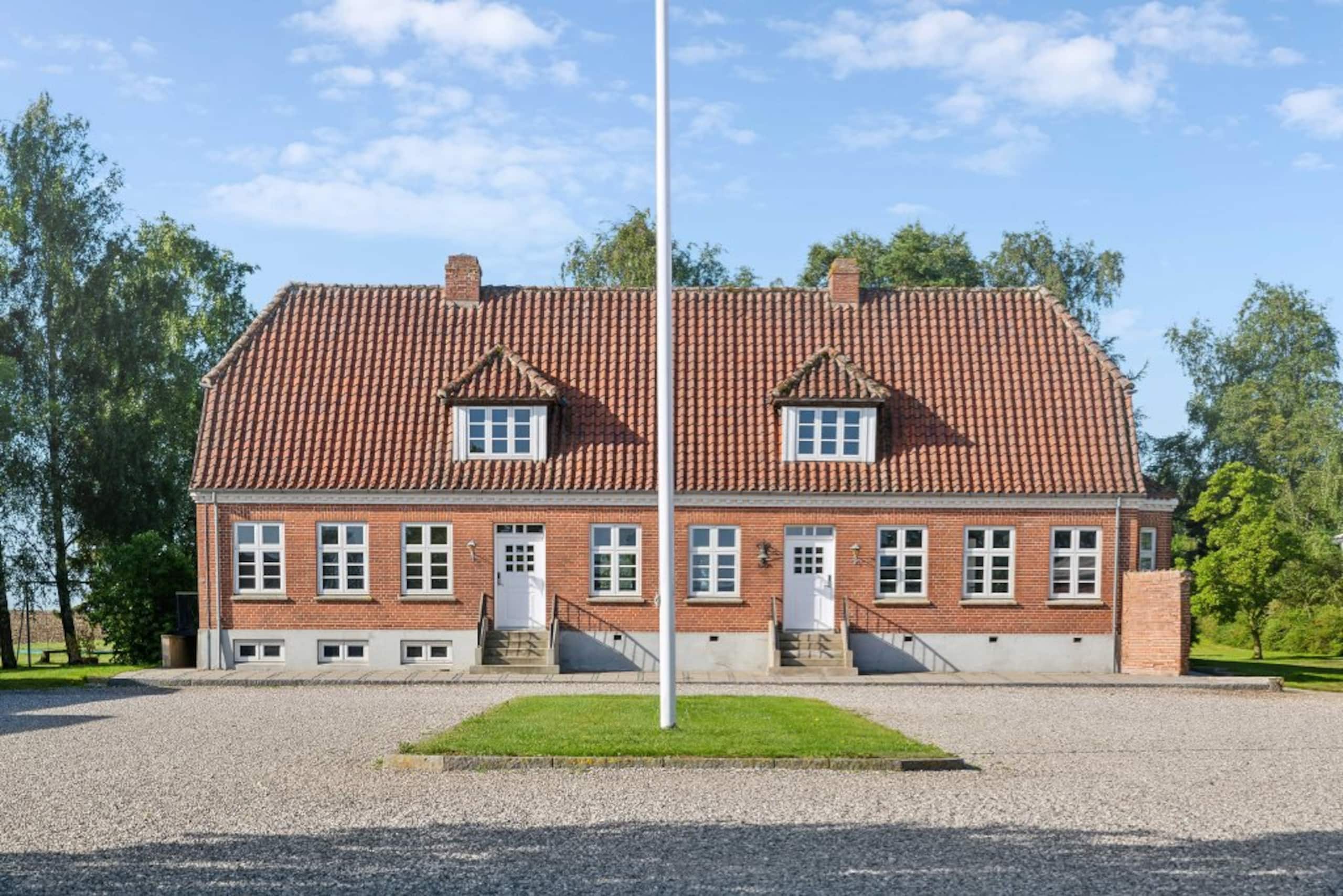 Hovedbygningens røde teglfacade med flagstang i sommersol