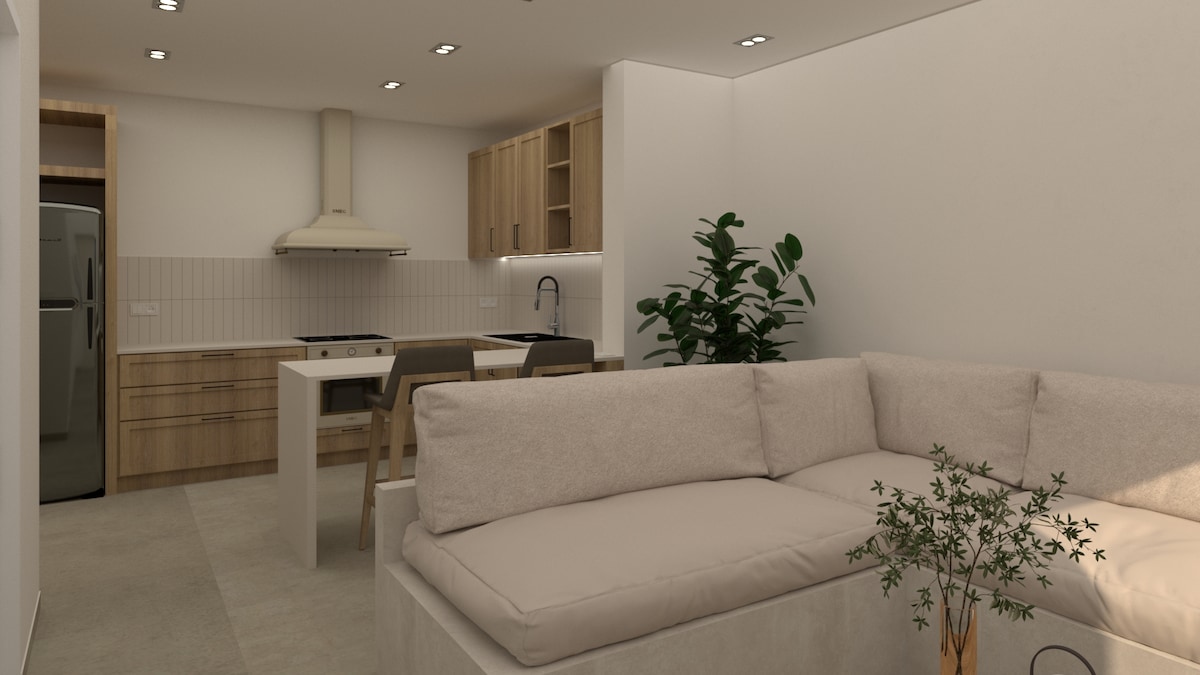 A modern kitchen area is complemented by light wood cabinetry and sleek appliances. A comfortable sectional sofa with neutral upholstery is positioned nearby, adding a cozy touch to the open living space. Potted plants enhance the fresh and inviting atmosphere.