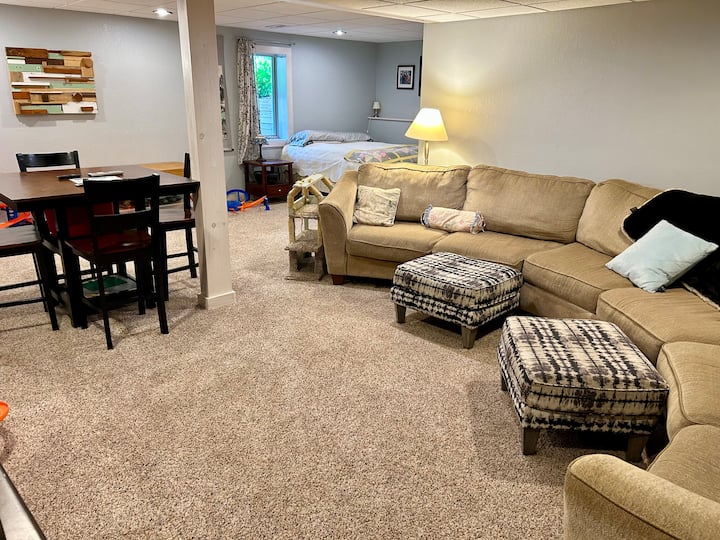 Ხედი ტელევიზორის კუთხიდან, რომელზეც დგას მაგიდა, ორადგილიანი საწოლი და ტახტი. Ფანჯარაში ოთახის გამუქებული ფერებია.