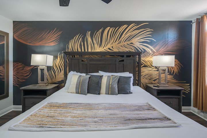 Elegantna i moderna spavaća soba s luksuznim bračnim krevetom i bijelom posteljinom koja pruža vrhunsku udobnost. Ova spavaća soba ima dovoljno prirodnog svjetla i ističe upečatljiv mural s tamnosivom pozadinom i elegantnim zlatnim perjem.