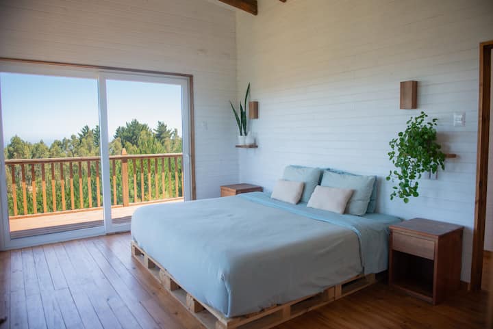 Habitación master con cama super king de 2 mts x 2 mts, balcón privado y una vista de ensueño. Dos ventanales gigantes que te dan vista desde el mar y el bosque de pinos. ¡Podrás disfrutar de las puestas de sol mas bellos que has visto en tu vida!