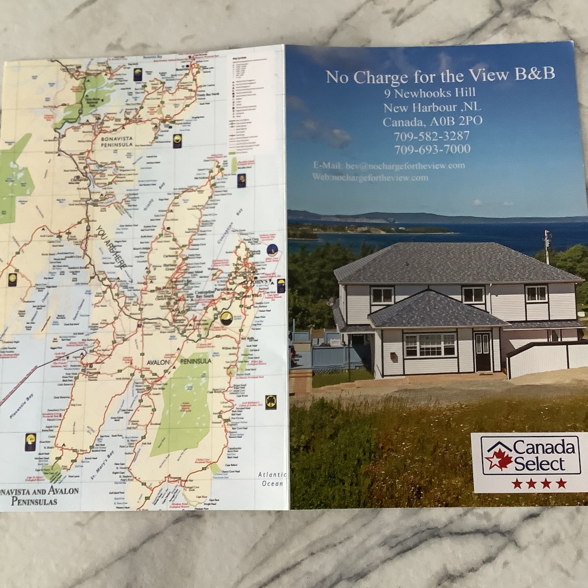 A folded brochure displays a detailed map of the surrounding area, highlighting key locations. The cover features an image of the accommodation, set against a backdrop of water and landscape. Contact information and a logo are prominently displayed, indicating the establishment's quality certification.