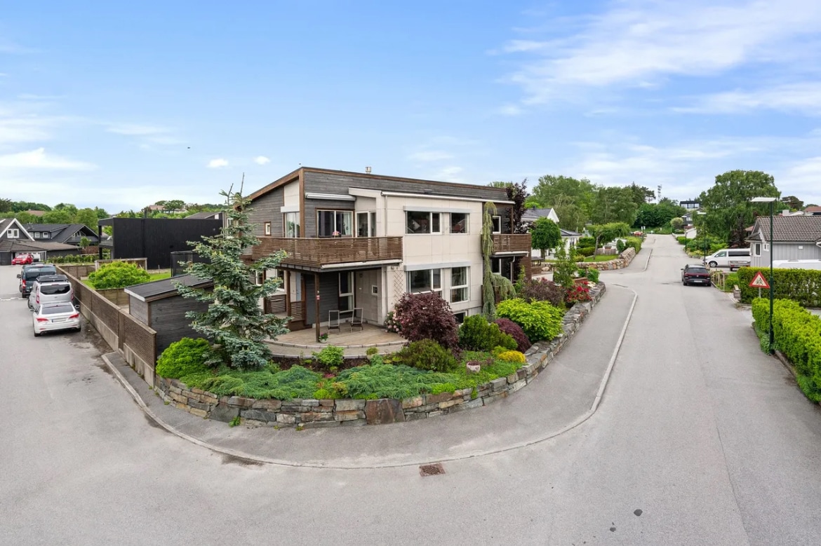 A modern two-story building is shown amidst a tree-lined street with well-maintained landscaping. Green shrubs and trees surround the property, enhancing the communal atmosphere. A circular driveway provides access to parking, while peaceful surroundings contribute to a serene environment typical of a family-friendly neighborhood.