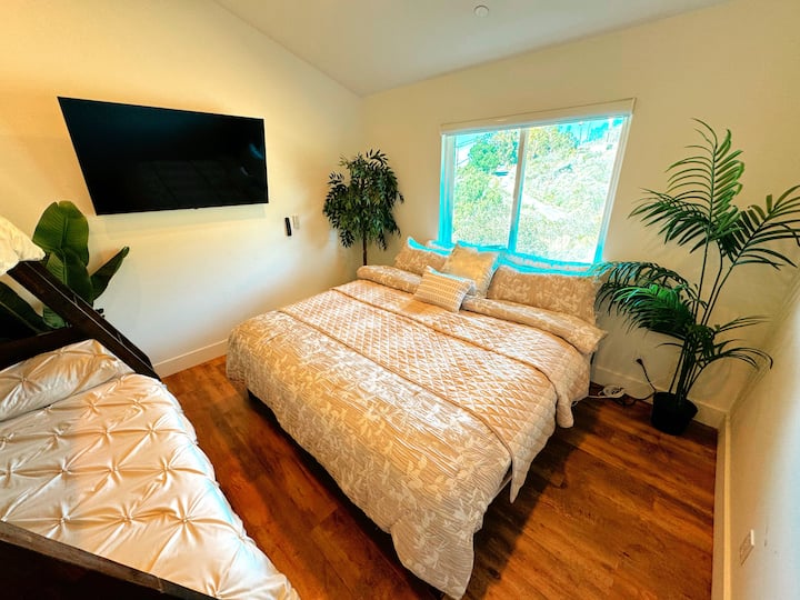 Kitanda aina ya King.  Dirisha lenye mwonekano wa mazingira ya asili.  Mimea mizuri kwenye kona ya chumba.  Televisheni ya LED imewekwa ukutani.  Kitanda cha ghorofa.  Luva nyeusi