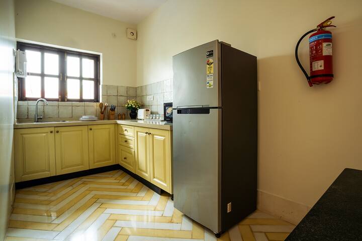 Bright and fully-equipped kitchen in our Goa villa, featuring a refrigerator, ample counter space, and charming yellow chevron floors for a delightful cooking experience.