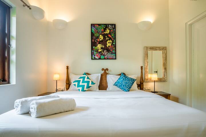Relax in style in this vibrant bedroom at our Goa villa, featuring a comfortable bed, eclectic art, and soft lighting for a perfect night's sleep.