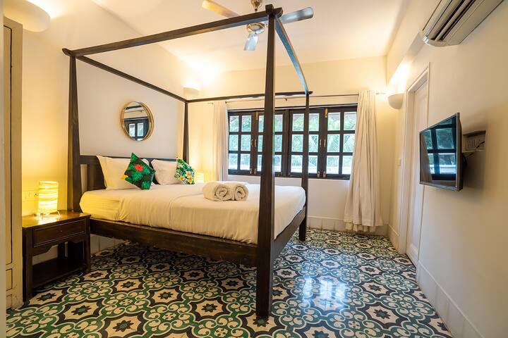 Cozy bedroom in our Goa villa featuring a charming four-poster bed, vibrant patterned floor tiles, and a smart TV for your comfort and entertainment.