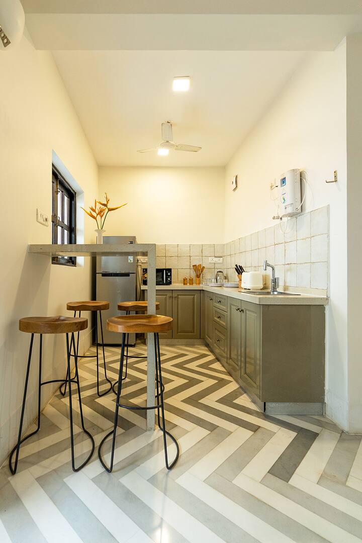 Fully equipped kitchen in our Goa villa, featuring modern appliances, a breakfast bar with seating, and stylish chevron flooring, perfect for your culinary adventures.