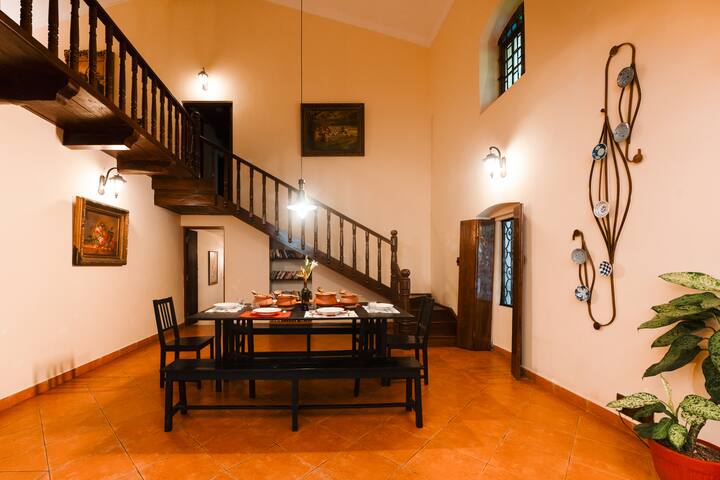 Nestled in Goa, this charming villa features a spacious dining area, a grand wooden staircase, and artistic décor, perfect for a memorable stay.