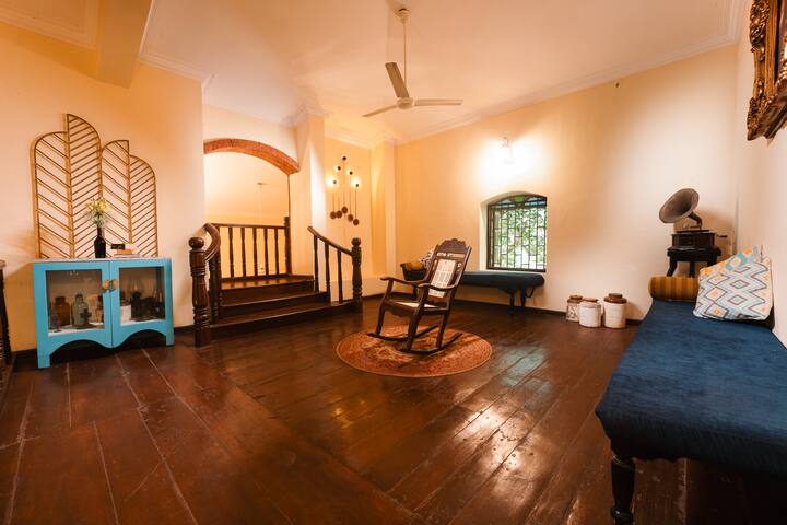 Step back in time in our Goa villa's grand common area, with vintage décor, a rocking chair, and a classic gramophone, perfect for relaxing.
