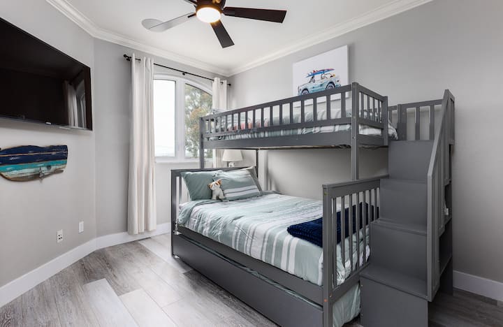 Спалня на горния етаж с двуетажно легло и разтегателна въртележка.  Разполага с 2 двойни/двойни легла и 1 единично/единично легло.  Смарт телевизор и дрешник. Тази спалня, друга стая и обща баня са на 3 - то ниво на дома (надолу по коридора от основната спалня). 