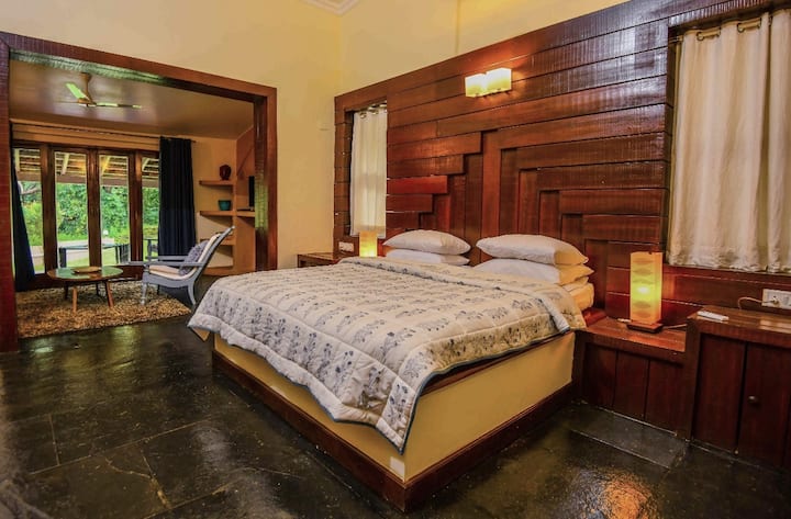 Step into comfort at this 5BHK Luxury Villa in Goa. This spacious bedroom features a plush bed, rich wooden accents, and a connecting lounge area.