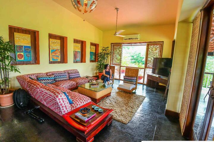 Discover the spacious living at our 5BHK Luxury Villa in Goa. Relax on vibrant sofas, enjoy charming artwork, and soak in the natural light: your perfect Goan retreat.