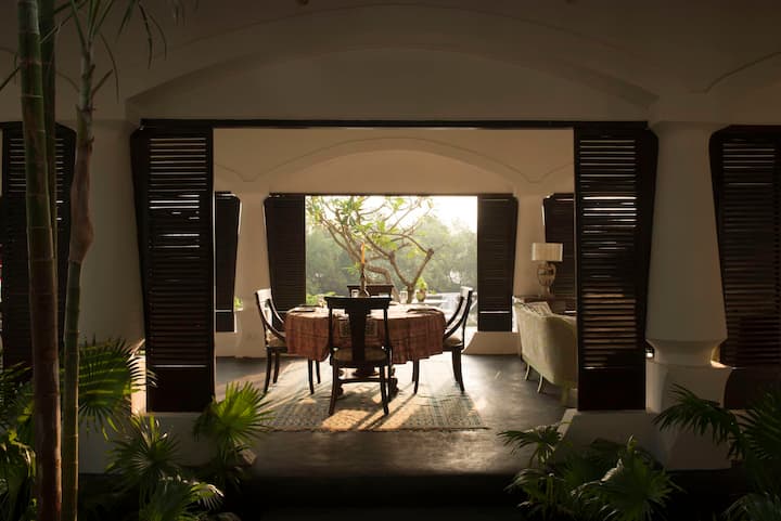 Escape to our serene Luxury Villa in Goa. This beautiful outdoor patio, surrounded by lush greenery, is the perfect spot for dining al fresco or enjoying a quiet moment in nature.