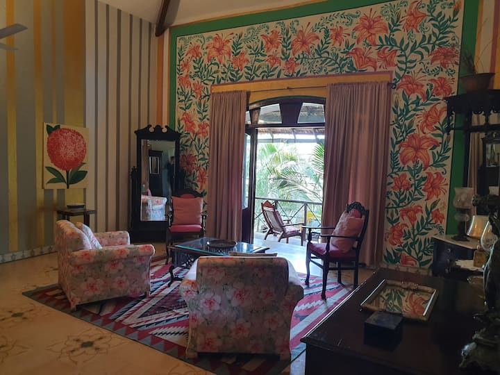 Step into the vibrant living area of our Luxury Villa in Goa. This unique space features artistic walls, plush seating, and a balcony with beautiful views, perfect for a relaxing and stylish getaway.