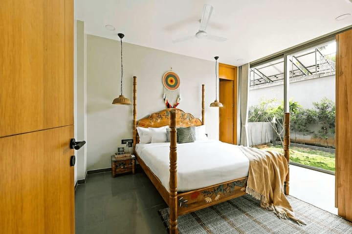 Experience comfort in this cosy bedroom at our Goa villa, featuring a charming four-poster bed and direct access to a serene private garden view.
