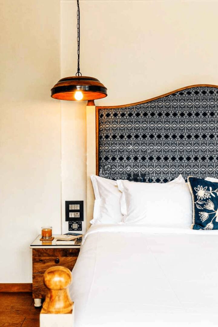 Close-up of a stylish bedroom in our Goa villa, showcasing the unique patterned headboard, warm lighting, and a charming bedside setup for your comfort.