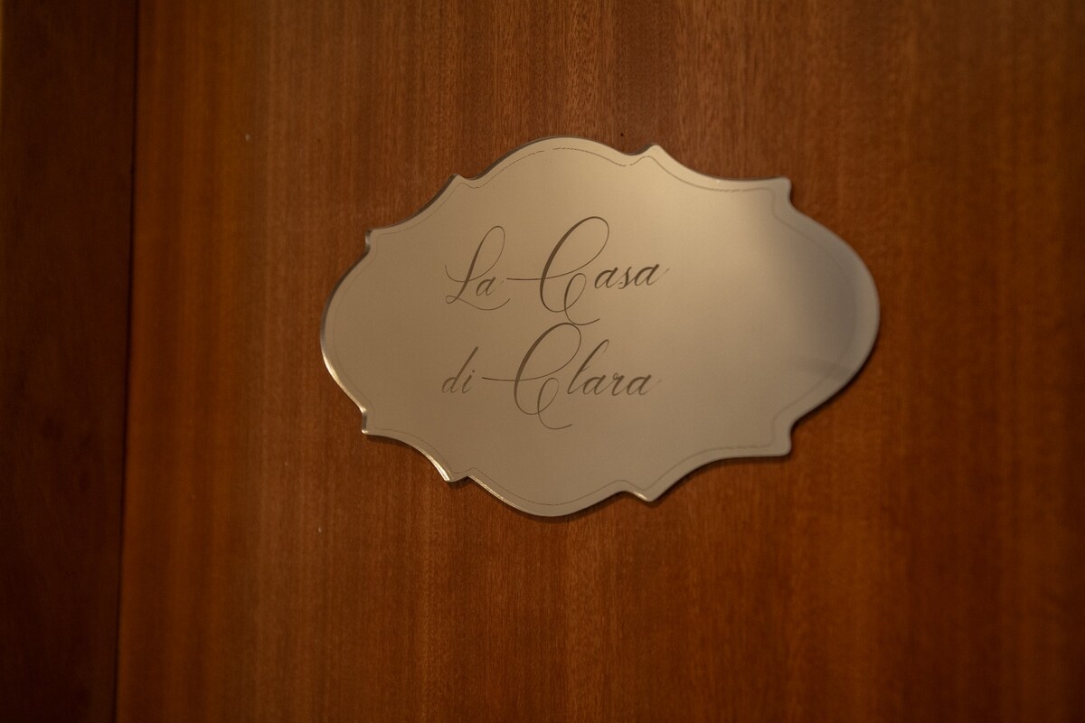 A polished wooden door showcases a decorative nameplate. The nameplate features elegant script that reads 'La Casa di Clara,' contributing to a welcoming entryway. The warm tones of the wood highlight the charm of the entrance.