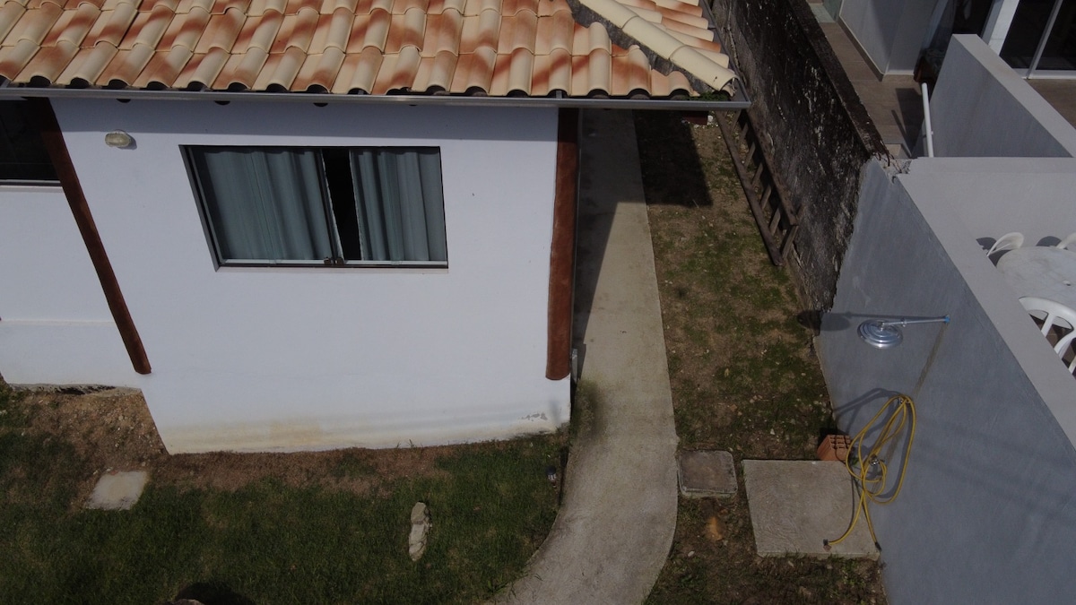 An aerial view captures the exterior of the property, featuring white walls and a tiled roof. A curved pathway leads from the house to the grassy area, with visible outdoor seating and a outdoor shower nearby, creating a welcoming outdoor space.