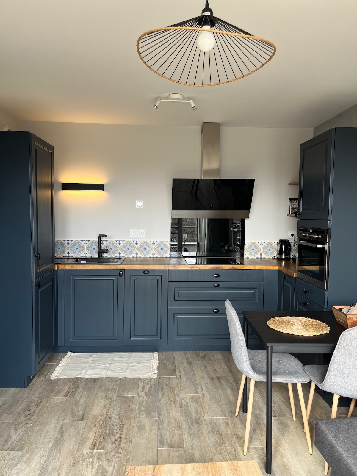 The kitchen is organized with dark cabinetry and a stylish countertop, featuring modern appliances including an oven and microwave. A dining table with four chairs is placed near the window, while patterned tiles add character to the space. A pendant light hangs from the ceiling.