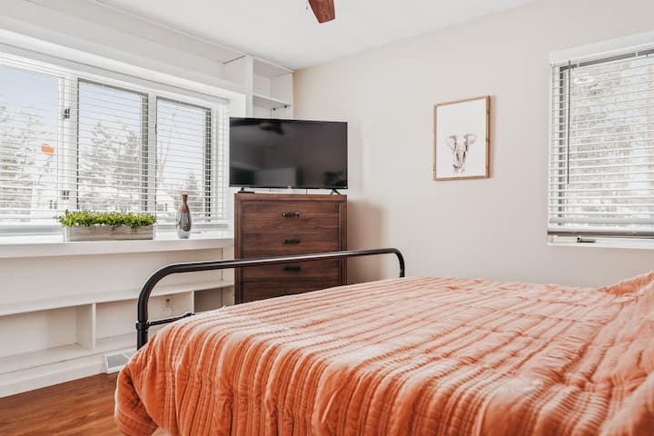 Bright and airy bedroom with a comfy bed, sunny windows, and a TV — your perfect room to relax and recharge!