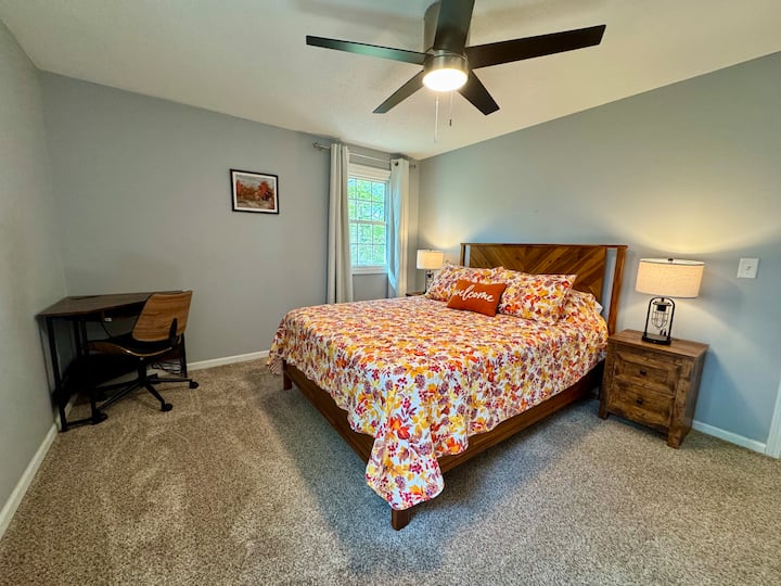 The fall-themed bedroom features vibrant colors, a comfortable queen-sized bed, and a designated workspace, perfect for both relaxation and productivity.