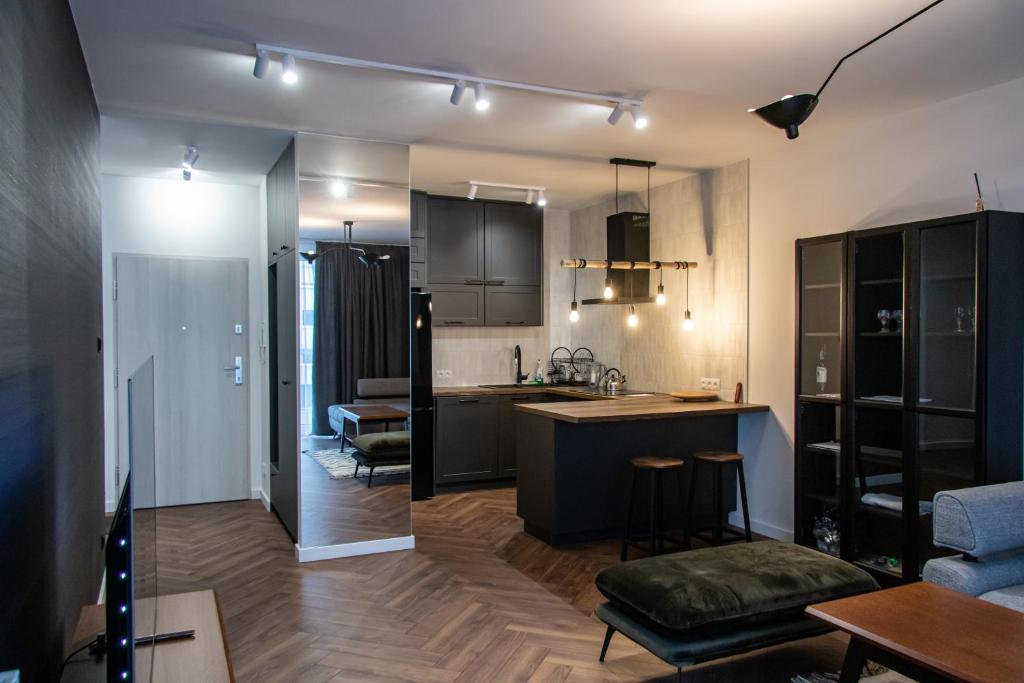An open-plan living area features modern cabinetry and a kitchen island with seating. Warm wood flooring runs throughout. The space is illuminated by industrial-style lighting, and a cozy seating area lies adjacent, offering a blend of comfort and contemporary design.