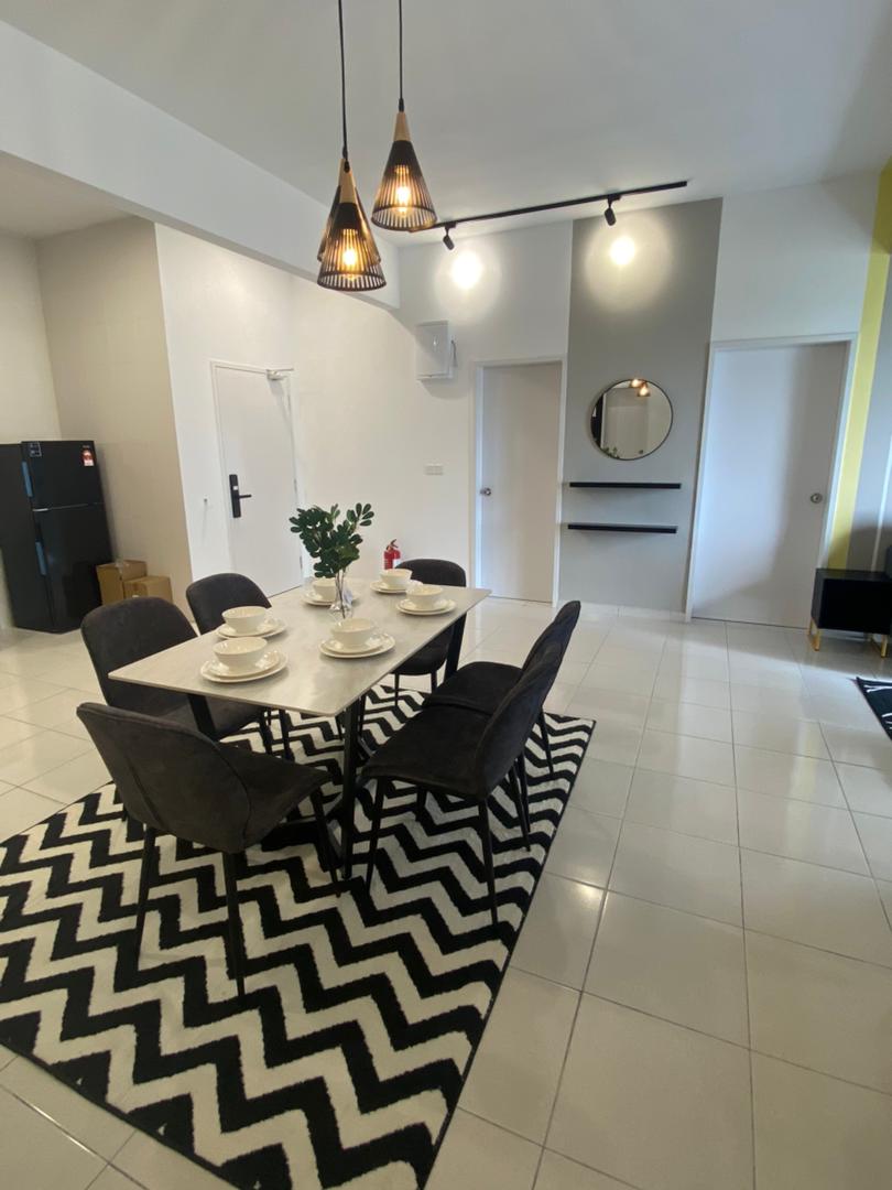 A dining area features a rectangular table set for four, complemented by dark, cushioned chairs. A patterned black and white rug grounds the space, while modern pendant lights hang overhead. The adjacent walls are minimally adorned, allowing focus on the arrangement.