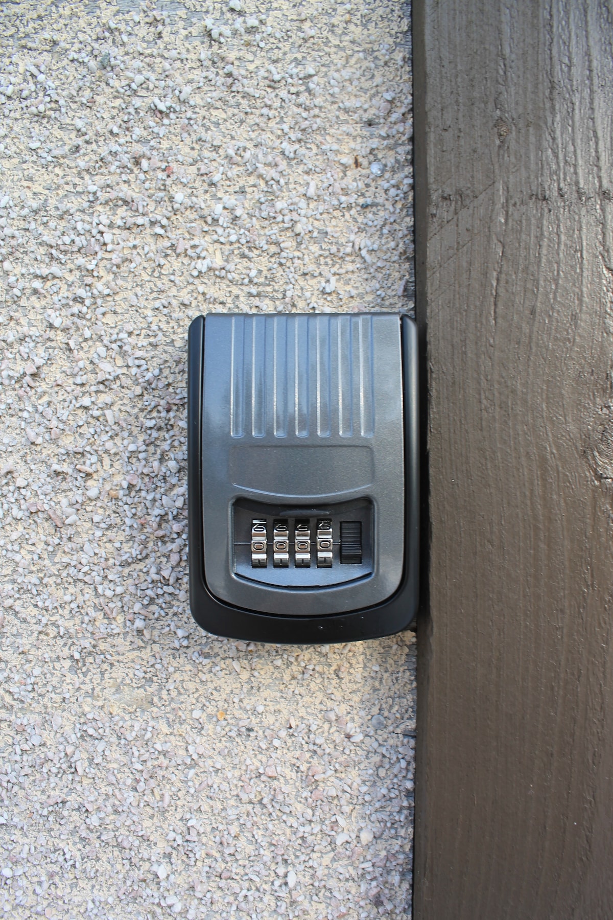 A secure key lockbox is mounted on a textured wall. The lockbox features a numeric keypad, and its dark surface contrasts with the light-colored wall. This allows for easy access to the property key while ensuring privacy.