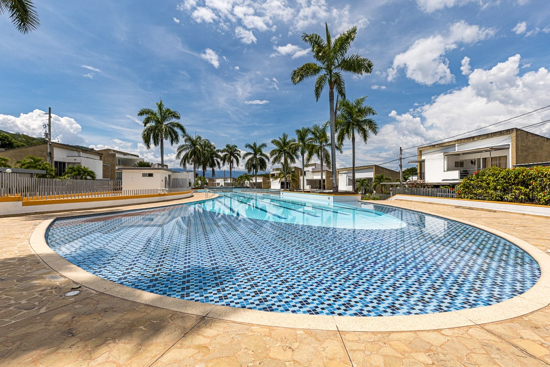 An expansive swimming pool is featured, showcasing a unique mosaic pattern on the bottom. Palm trees line the area, contributing to a tropical ambiance. The surrounding pool deck is paved with light-colored tiles, offering ample space for sunbathing or relaxation.