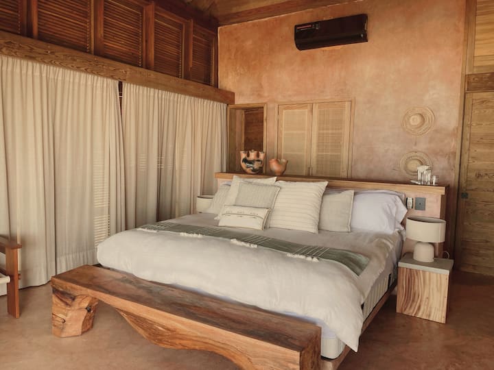 - Un dormitorio sereno con madera natural y decoración tejida   - Tonos neutros y tejidos suaves que invitan a un descanso profundo   - Un espacio tranquilo y conectado a tierra para noches apacibles  