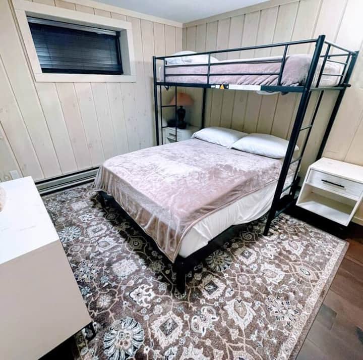 A cozy bedroom featuring a black metal bunk bed with a plush double bed below and a single bed on top.