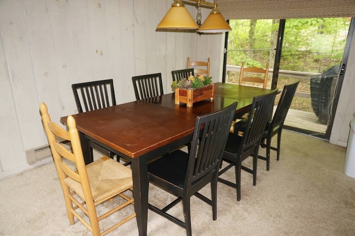 A rustic dining area with a wooden table, mismatched chairs, and warm lighting, set against a cozy cabin-style backdrop.