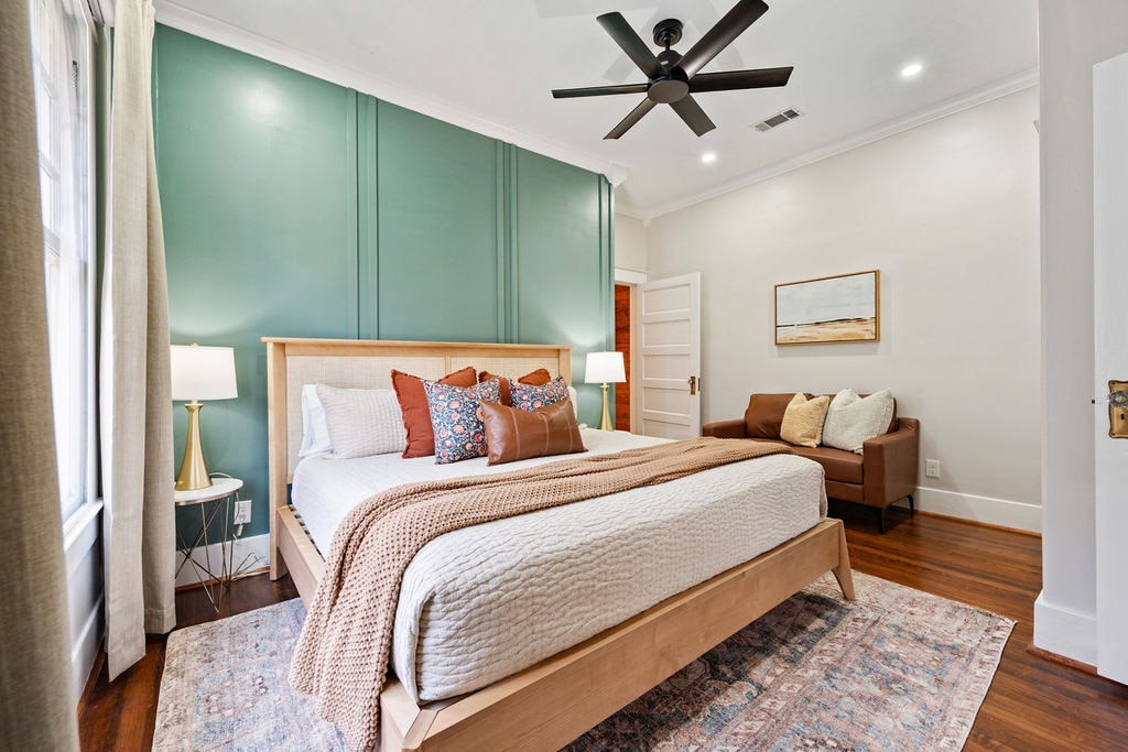חדר שינה ראשי עם מיטת קינג סייז, מנורות עם שקעים ויציאות USB לטעינת טלפון, מאוורר תקרה ומושב מפואר למנוחה או לצפייה בטלוויזיה.
