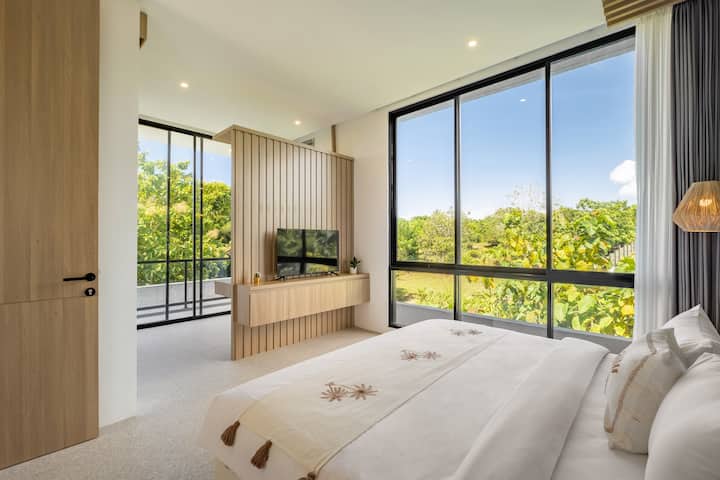 Светла и уютна спалня с панорамна гледка към зелени площи и акценти от естествена дървесина.