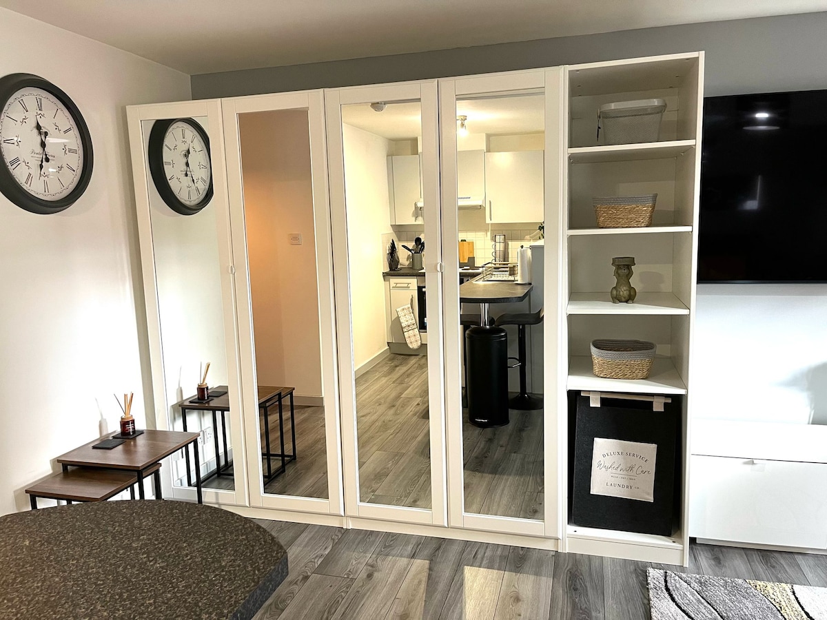 A stylish storage unit features mirrored doors and open shelving, enhancing the space's functionality. The area includes two wall clocks and a small table, contributing to the modern aesthetic. In the background, a glimpse of the kitchen and dining area can be seen.