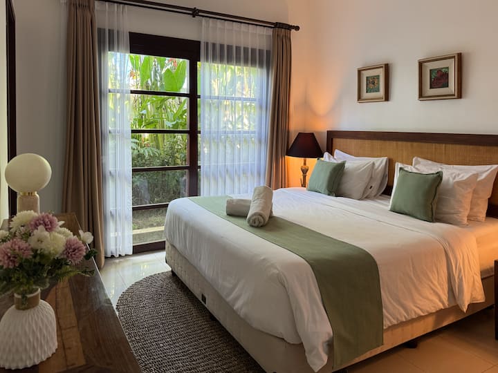 Amplio dormitorio tamaño queen con iluminación suave y acceso al jardín para una estancia tranquila en la villa de Bali.