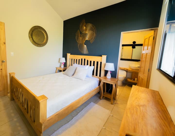This inviting bedroom features a cozy queen size bed framed by elegant handmade wall art crafted by a local artist, adding a unique cultural touch. Enjoy the added convenience of a private en-suite bathroom, perfect for comfort and privacy.
